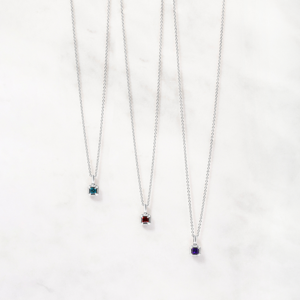 A rhodium-plated sterling silver necklace with a square-shaped pendant featuring a red garnet, set within a polished rounded square frame, with a chain visible in the background.