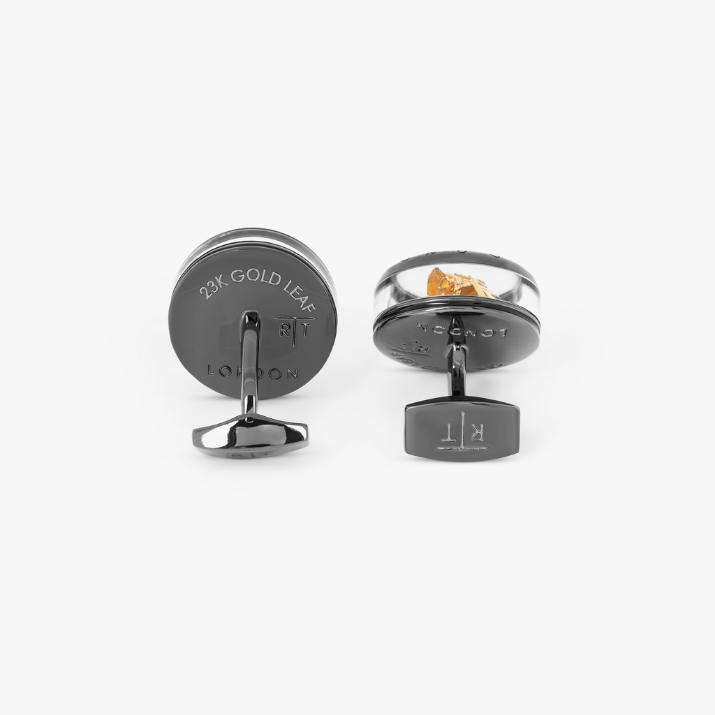 A pair of gunmetal finish cufflinks with black enamel detailing and gold leaf design.