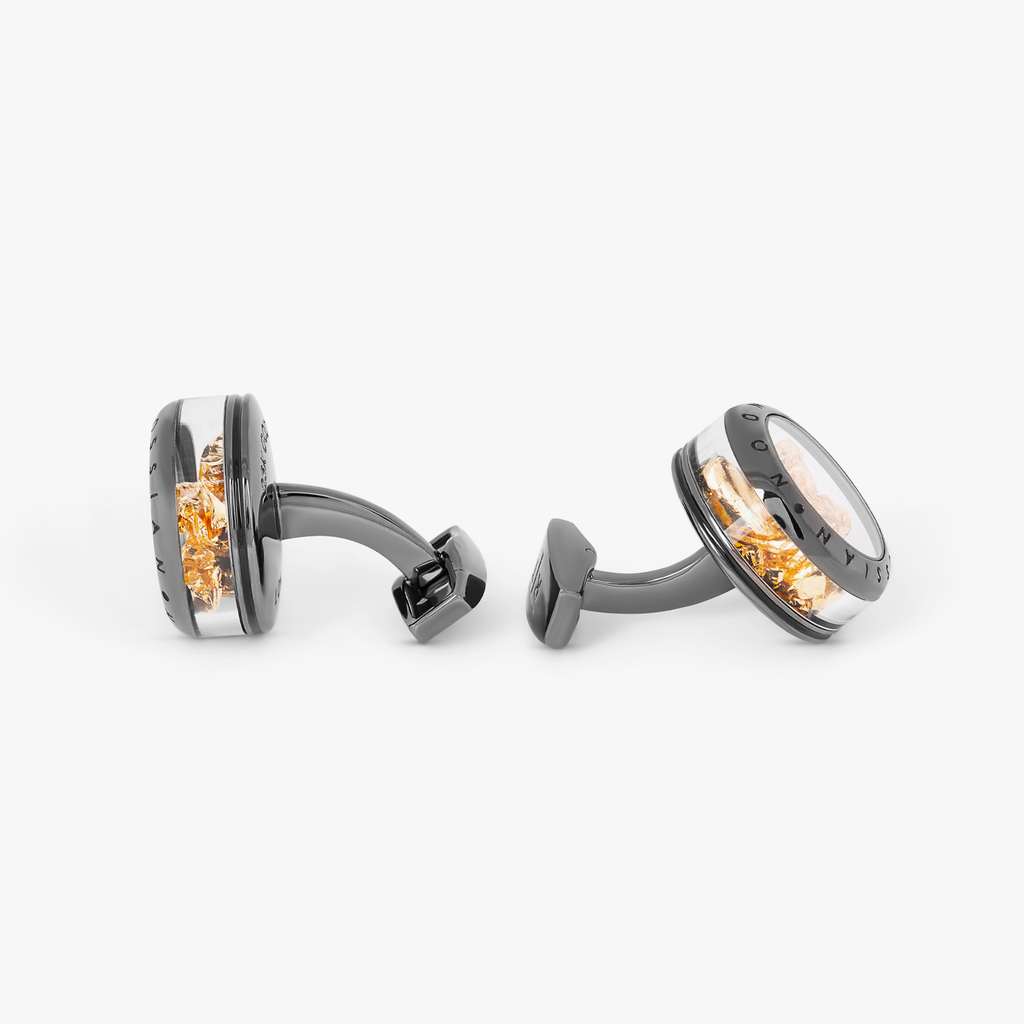 A pair of gunmetal finish cufflinks with black enamel detailing and gold leaf design.