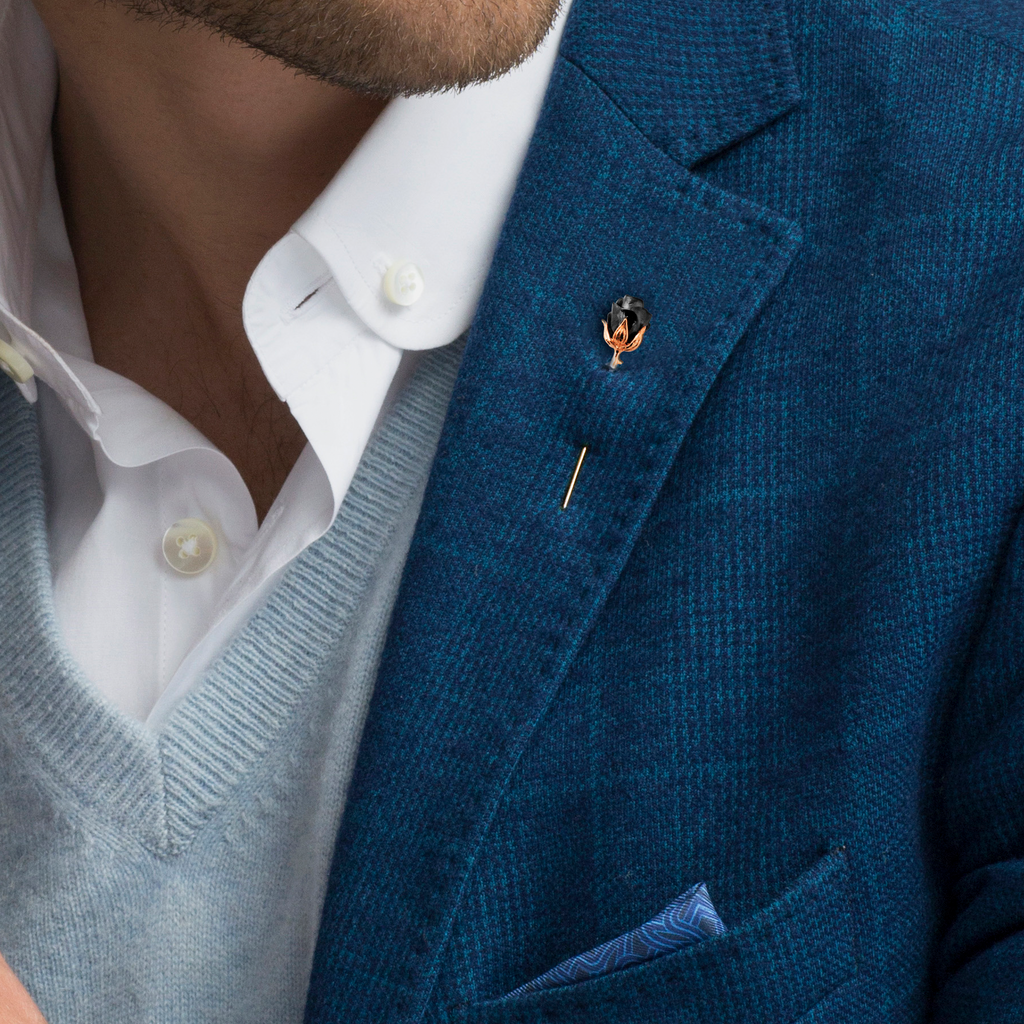 A rose-shaped lapel pin with a black enamel center, rose gold stem, and gunmetal accents.