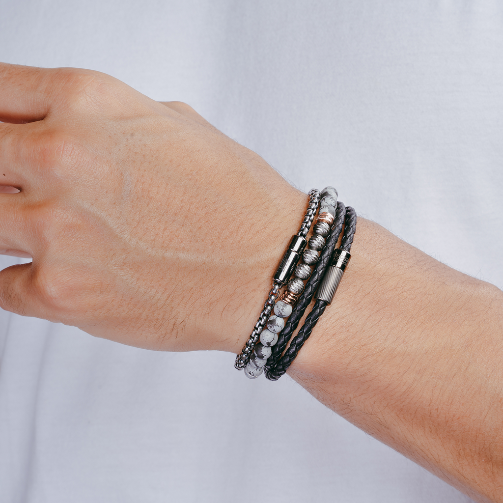 A black beaded bracelet with silver and rose gold-plated accents, featuring a snowflake obsidian stone and a small circular silver charm