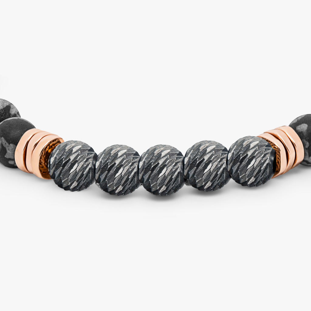 A black beaded bracelet with silver and rose gold-plated accents, featuring a snowflake obsidian stone and a small circular silver charm