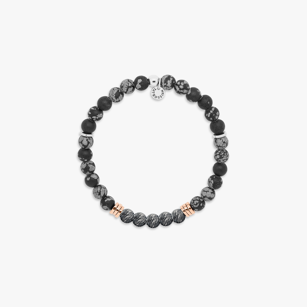 A black beaded bracelet with silver and rose gold-plated accents, featuring a snowflake obsidian stone and a small circular silver charm