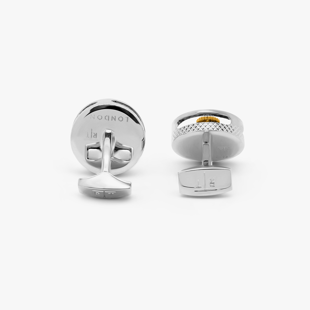 A pair of palladium-plated cufflinks with a round shape featuring rotating gear mechanisms and a black carbon fiber inlay.