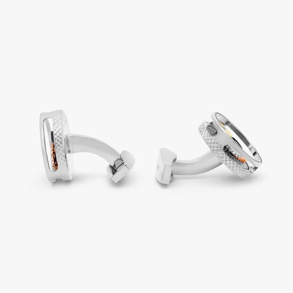 A pair of palladium-plated cufflinks with a round shape featuring rotating gear mechanisms and a black carbon fiber inlay.